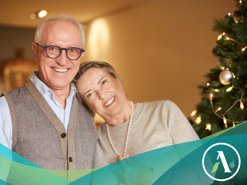 Happy senior couple smiles at camera with Christmas tree in the background.