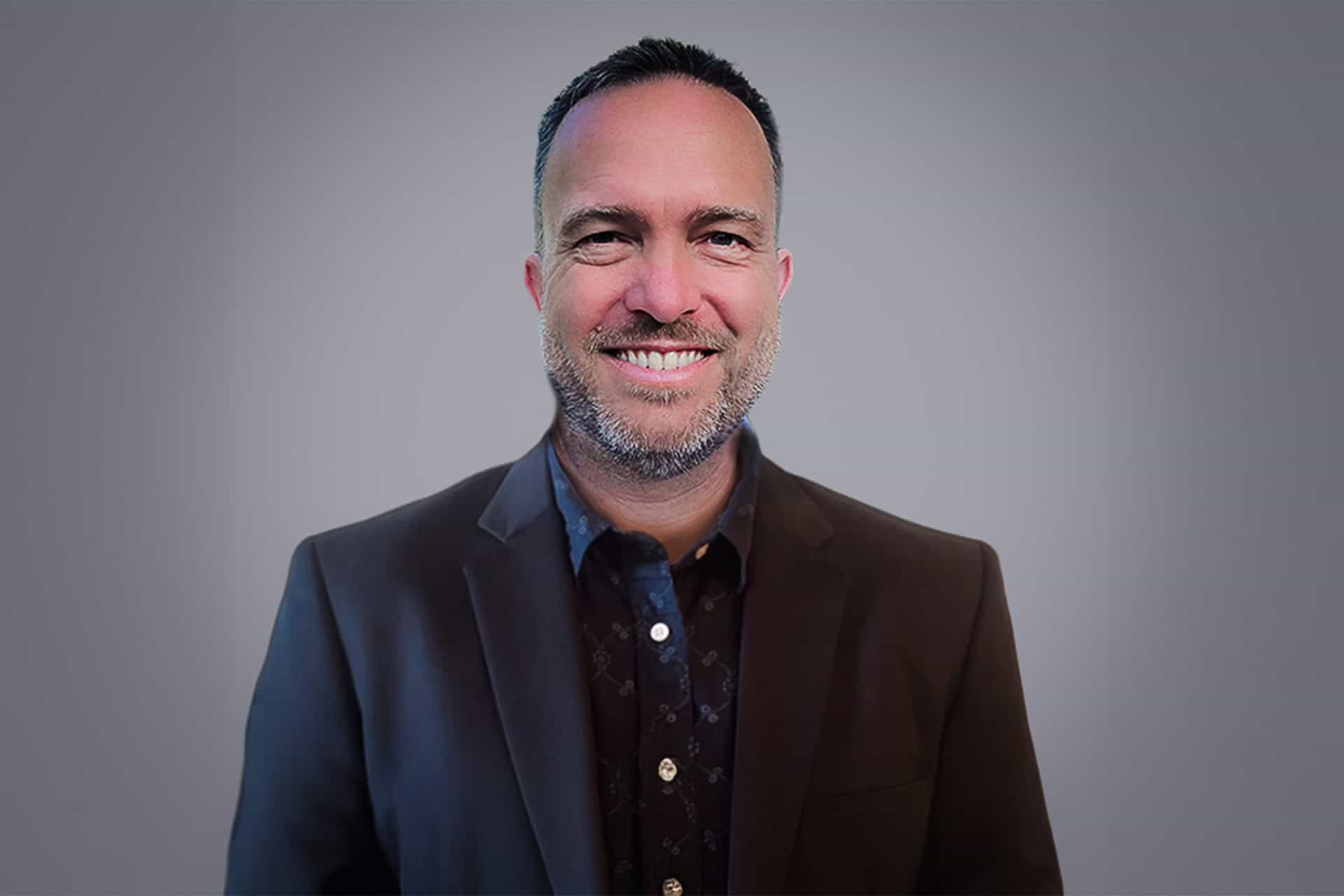 Brian Koning smiles at the camera against a solid grey background.