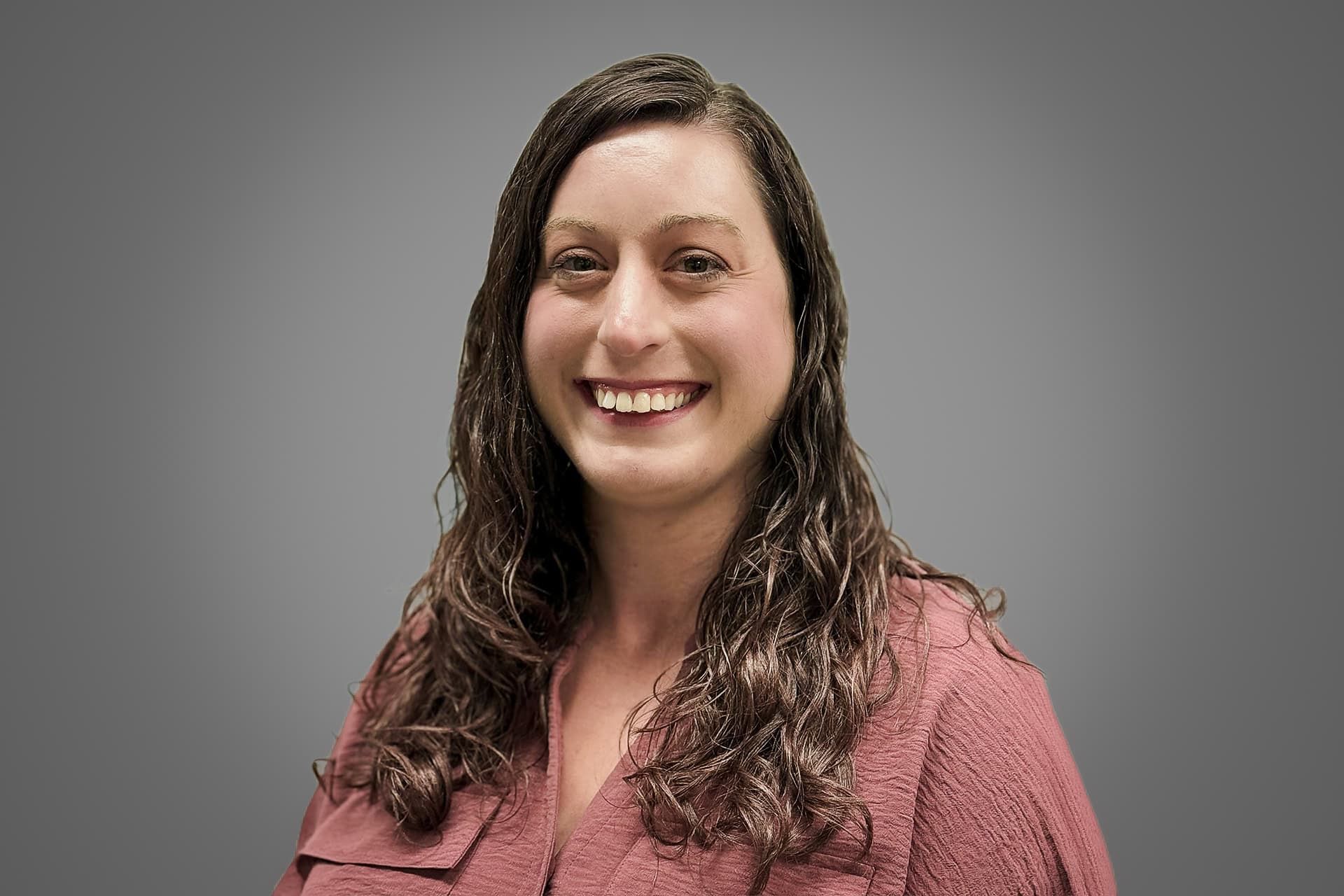 Ileane Baumgartner smiles at the camera against a solid grey background.